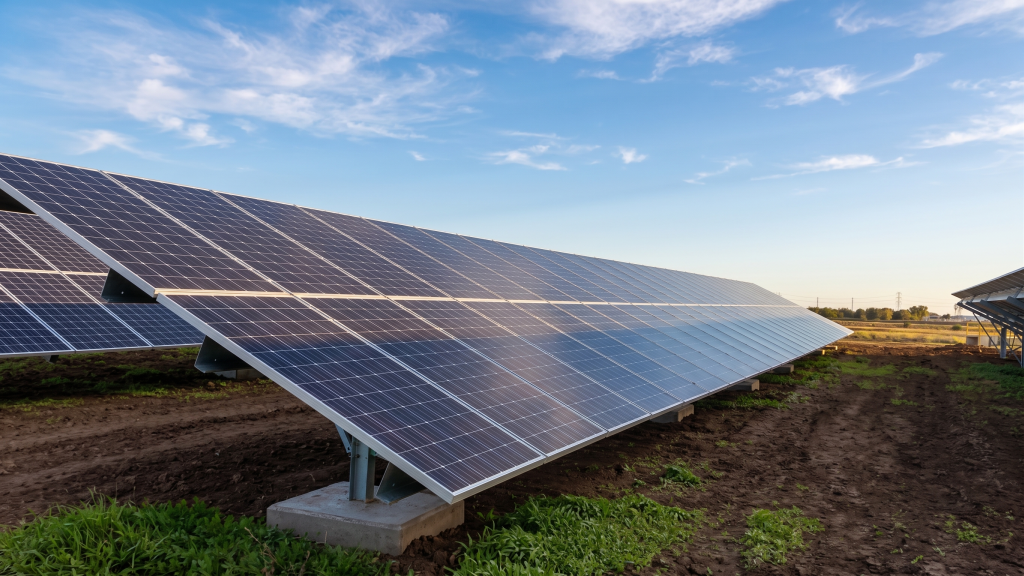 Large solar panels, part of municipal solar projects, are installed outdoors on sturdy metal frames above grassy and bare soil, with a bright blue sky and a few clouds in the background. Large solar panels, part of municipal solar projects, are installed outdoors on sturdy metal frames above grassy and bare soil, with a bright blue sky and a few clouds in the background.
