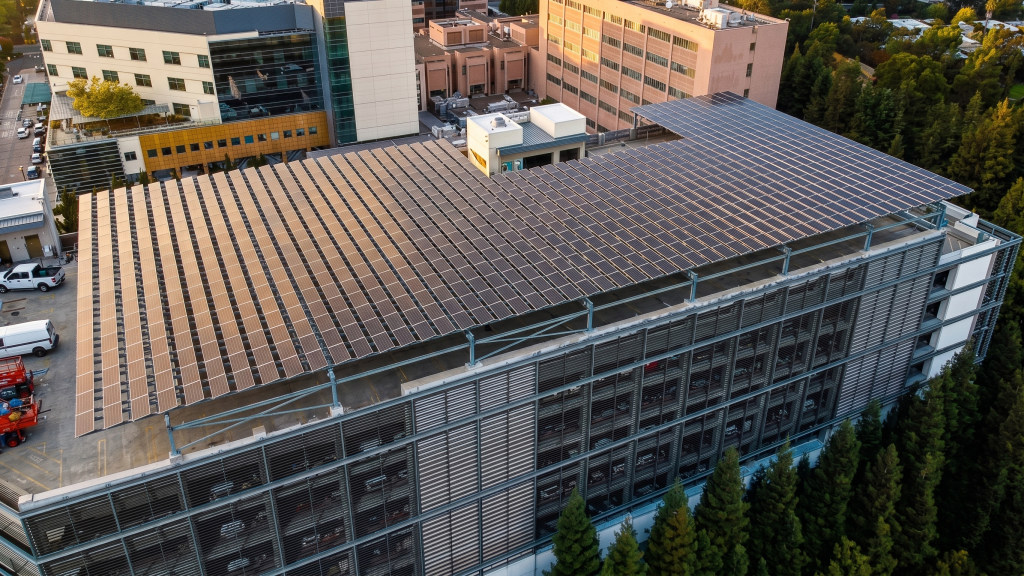 Aerial view of a large parking garage with a rooftop covered in solar panels installed through a Commercial Solar PPA, surrounded by office buildings and trees.